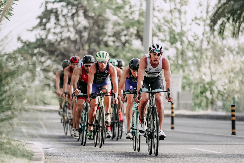 Full body of group of people in helmets and sportswear riding bicycles on asphalt road during race